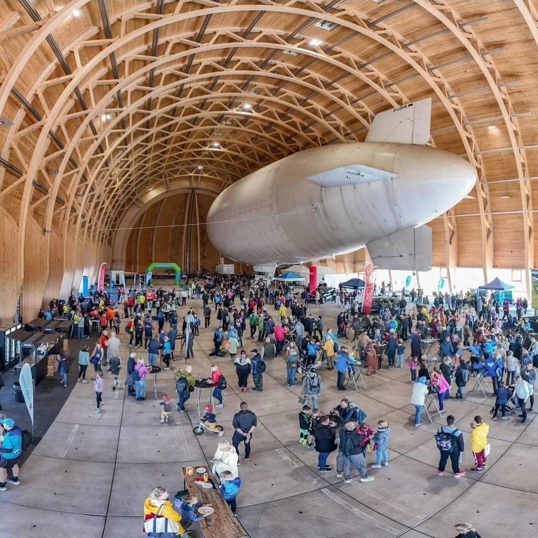 Volle Hangarhalle mit Zeppelin, Ständen und Zuschauenden
