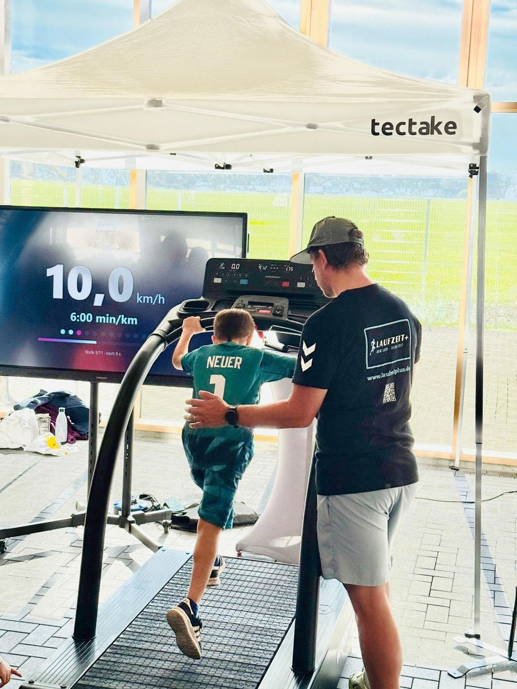 Ein Junge läuft bei der Kinder-Challenge auf dem Laufband, Tobi sichert ihn